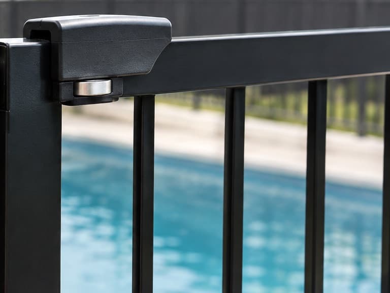 Close-up of a pool gate's magnetic latch at the top of the gate, with the pool behind